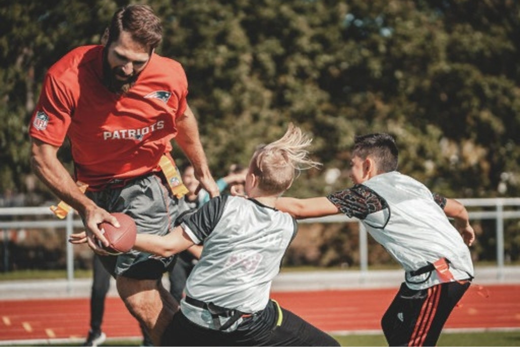 Sebastian Vollmer mit dem Ball beim Flag Football gegen zwei Kinder