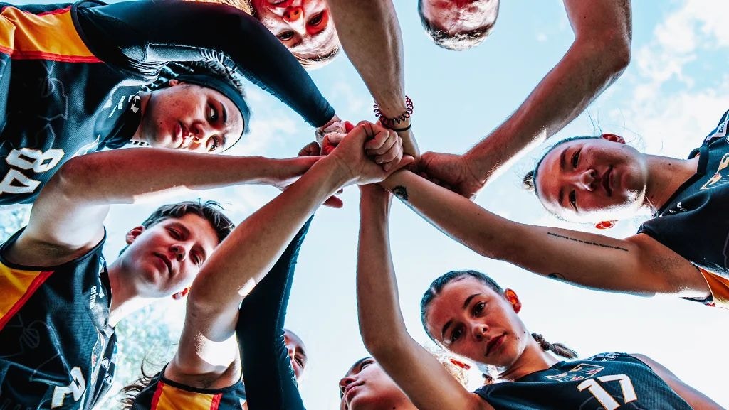 Spielerinnen der deutschen Flag-Football-Nationalmannschaft legen im Kreis die Hände zusammen, von unten fotografiert