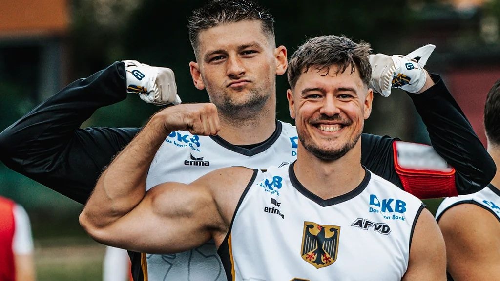 Zwei Spieler der deutschen Flag-Football-Nationalmannschaft der Männer lachen und spannen im weißen Nationaltrikot die Bizepse an