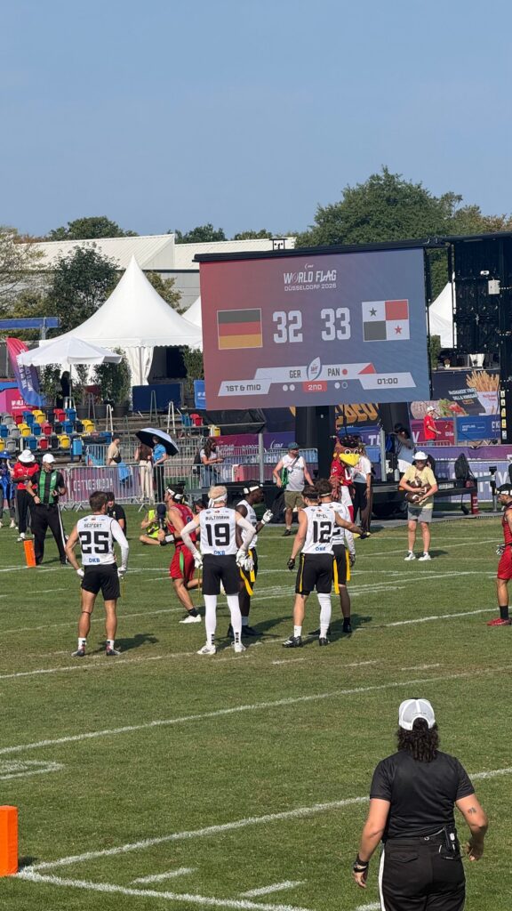 Flag-Football-WM 2026 in Düsseldorf: Spieler auf dem Feld, im Hintergrund die Anzeigetafel mit deutscher Flagge