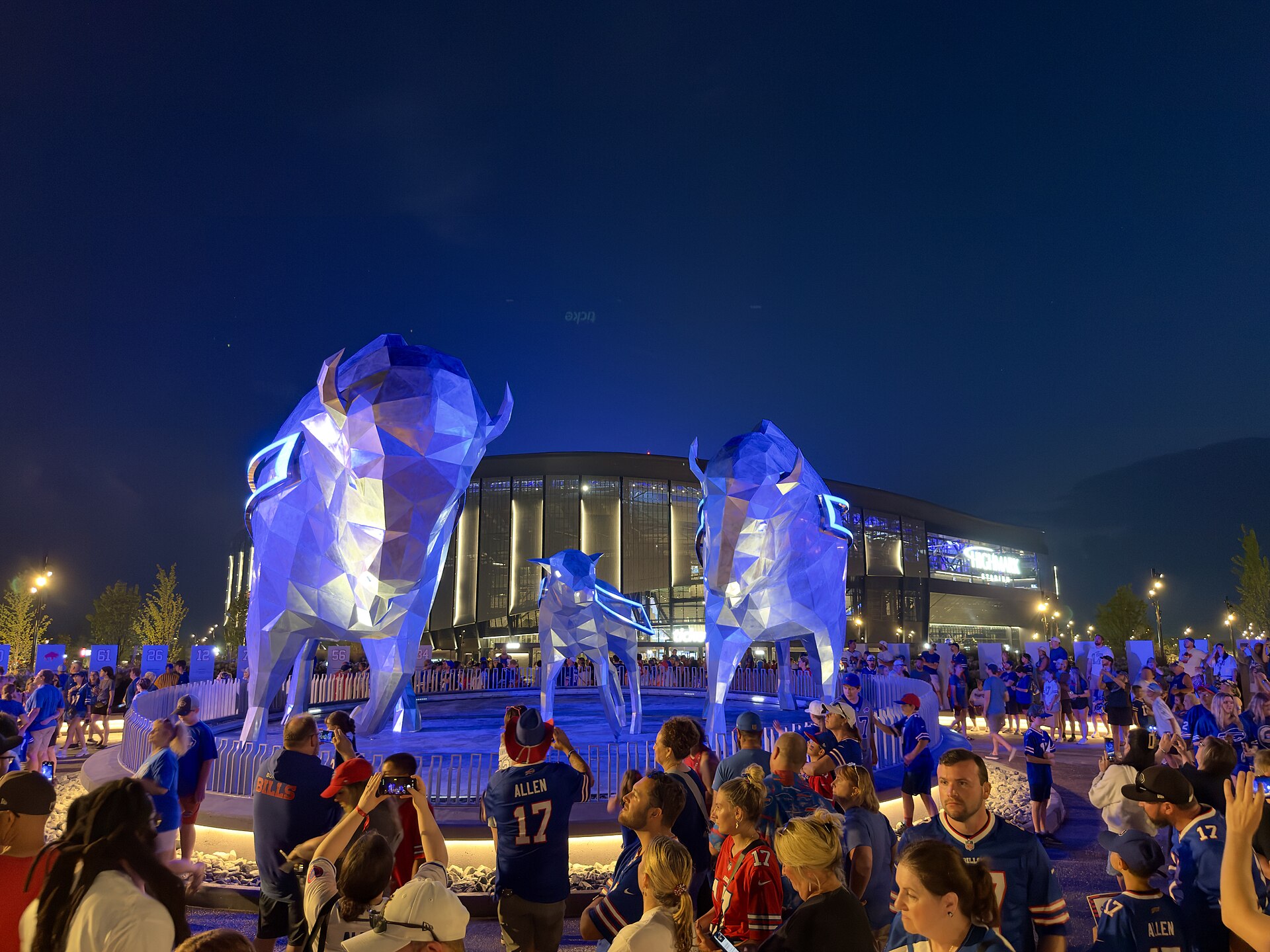 Blau beleuchtete Bison-Statuen vor dem neuen Highmark Stadium bei Nacht, davor Fans