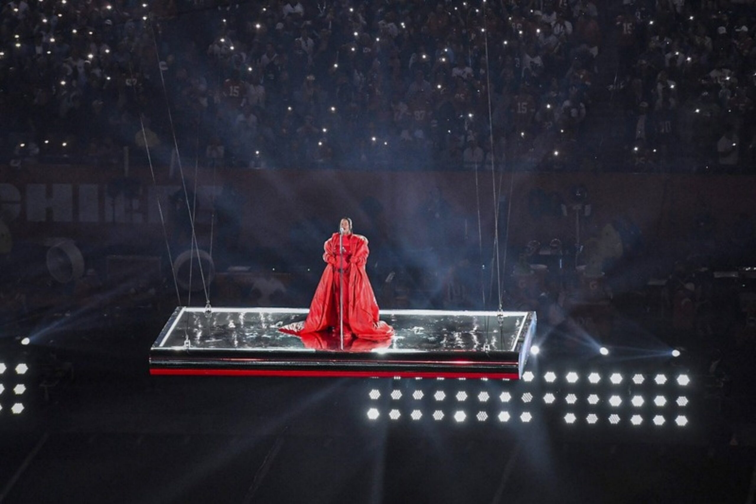 Rihanna im roten Outfit auf einer schwebenden Plattform über dem Rasen bei der Halftime Show des Super Bowl LVII